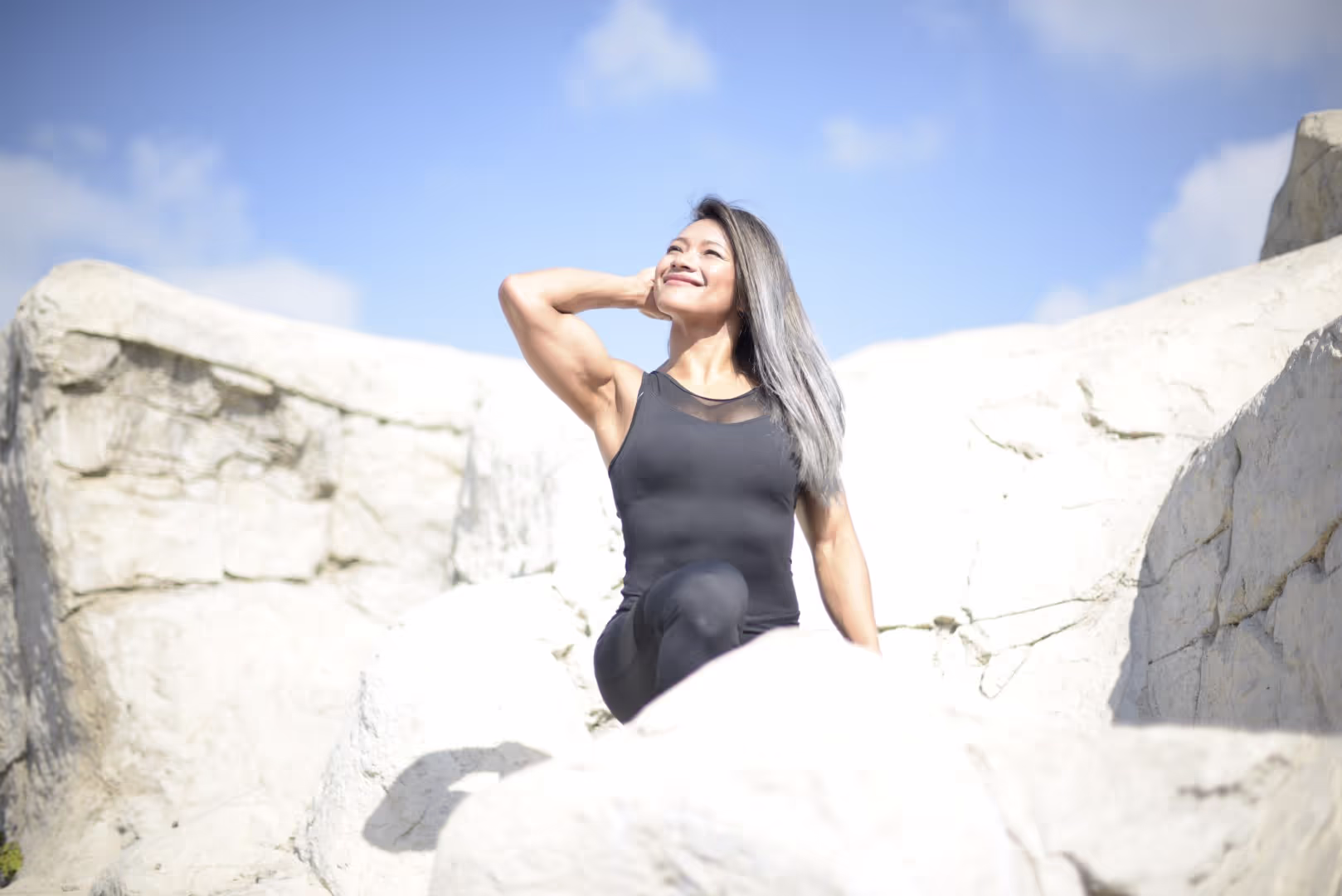 Smiling woman in black athletic wear posing on white rocky terrain under a blue sky.