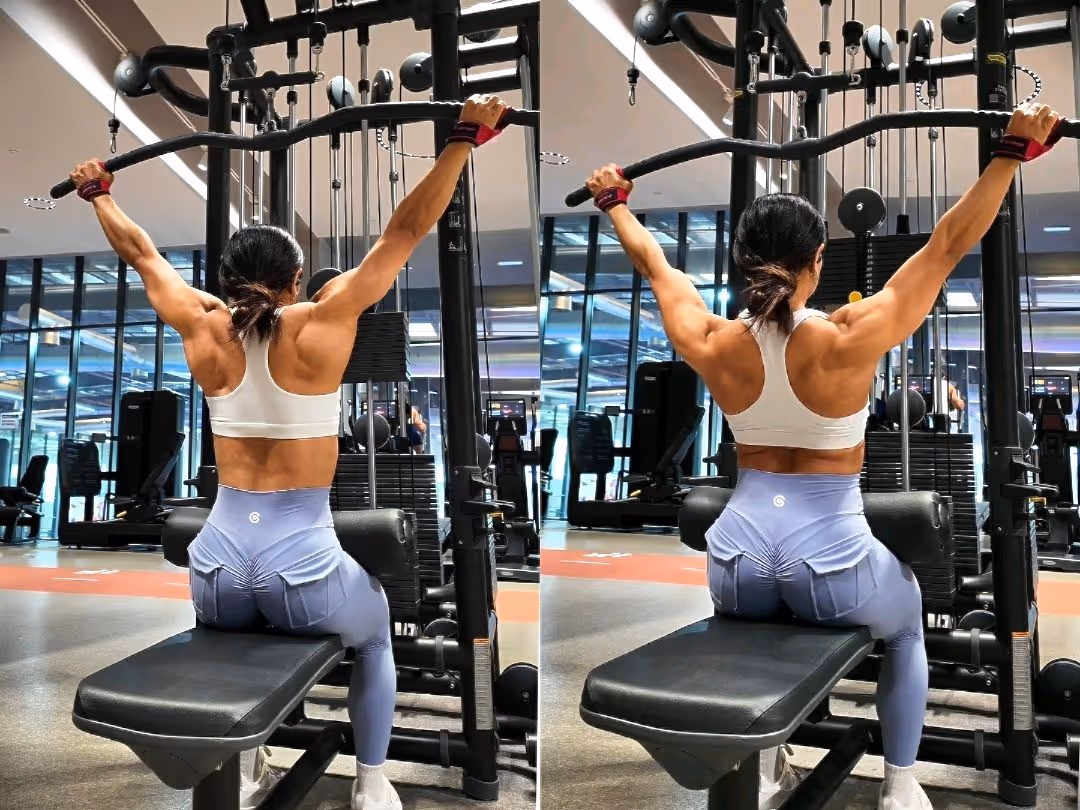Woman in white sports bra and blue leggings doing lat pulldown exercises on a machine in a gym.