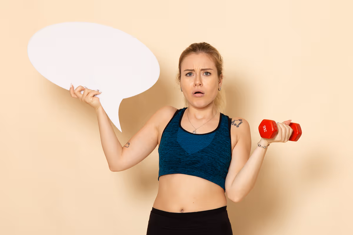 Confused woman in workout clothes holding a red dumbbell in one hand and a blank speech bubble cutout in the other.