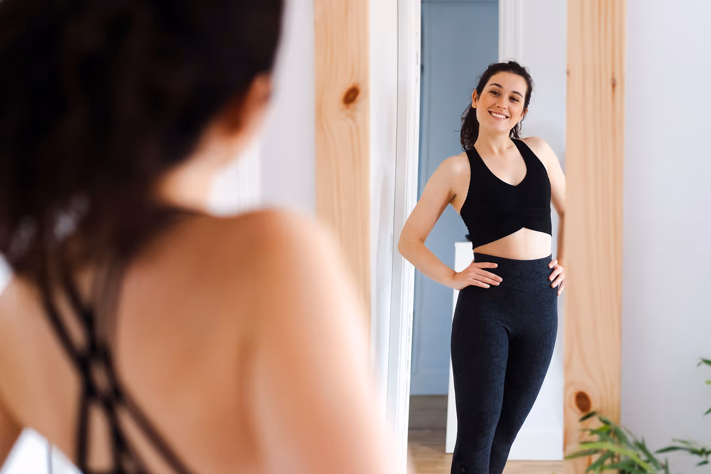 Smiling woman in black workout clothes posing confidently in front of a mirror.
